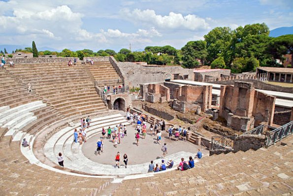 "Pompeii, Italy - July 24, 2012. Tourists mill about and sit and relax inside of the ancient Pompeii Amphitheatre. Pompeii was victim to the 79 A.D. eruption of Mount Vesuvius."